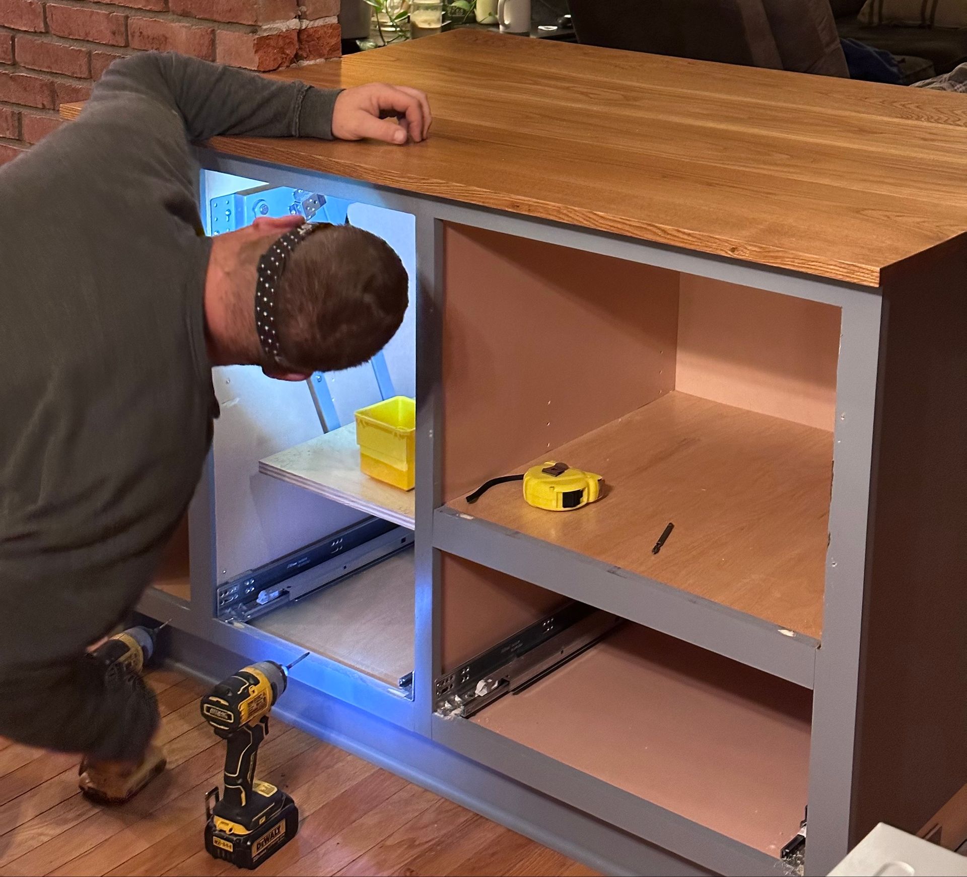 Man working on a wooden cabinet, using a drill, indoors.