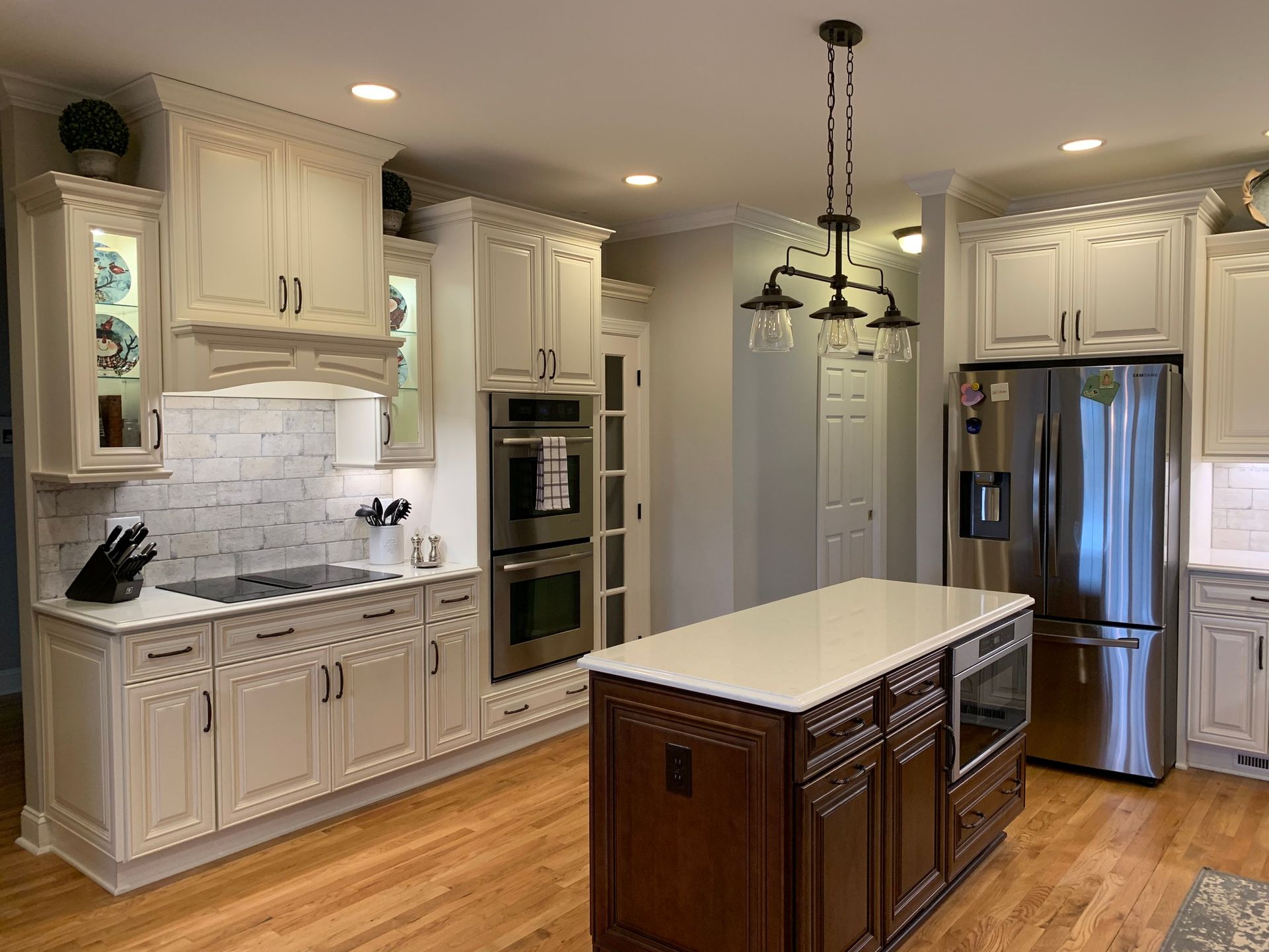 Cream-colored kitchen with a dark wood island. Stainless steel appliances, hardwood floors, and overhead lighting.