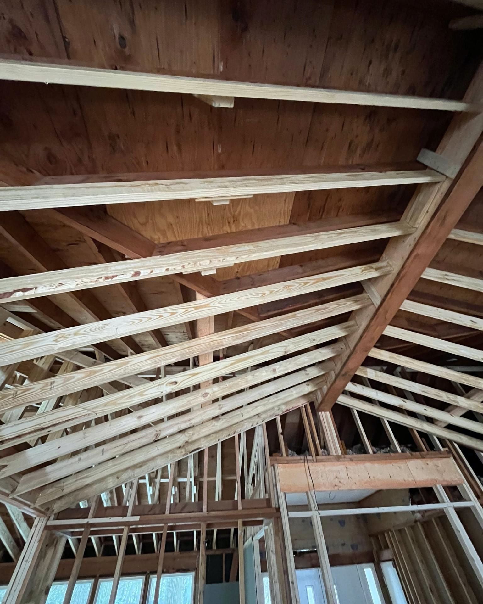 Interior view of a wooden house frame under construction; exposed rafters, plywood ceiling.
