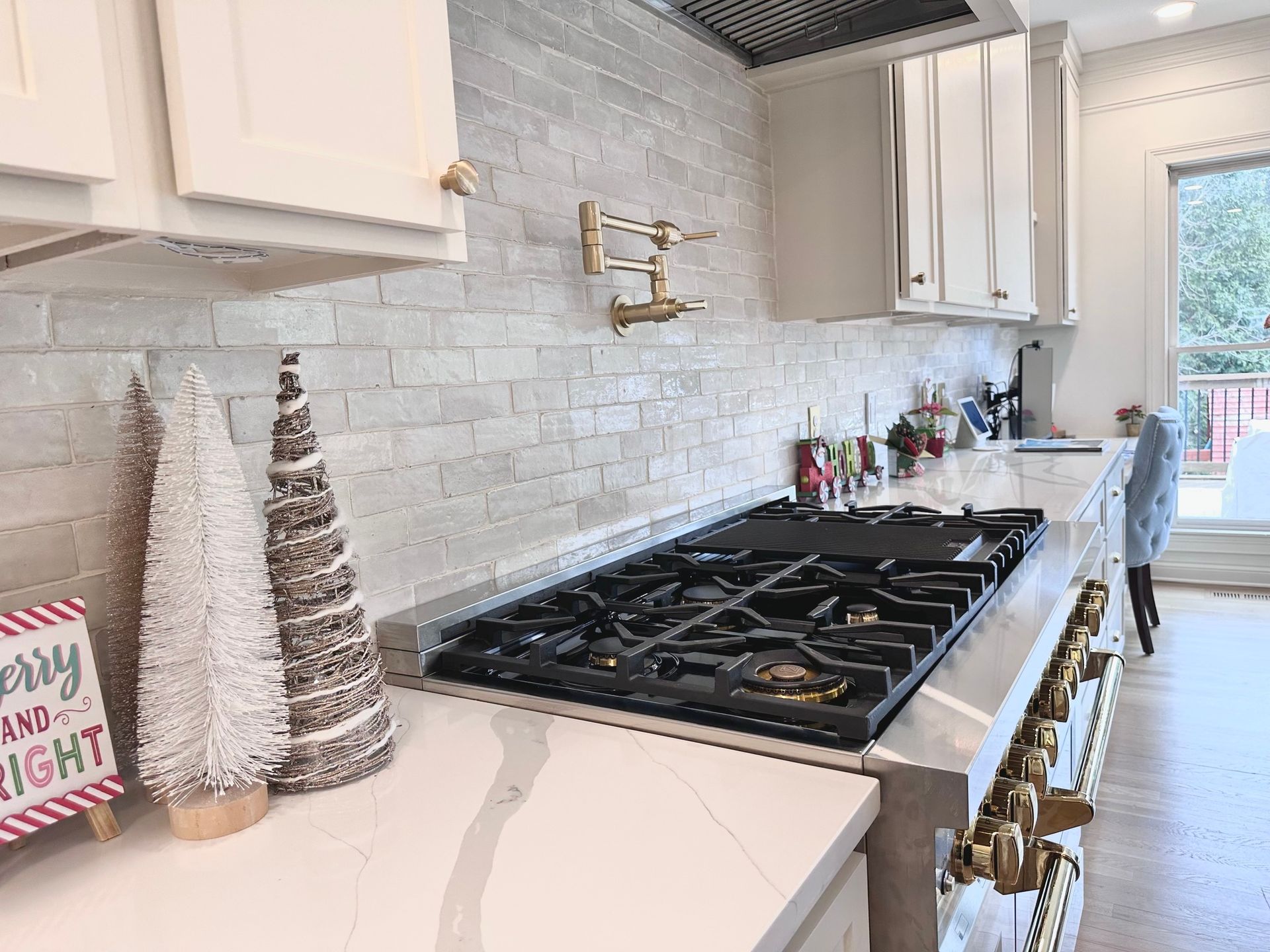 Kitchen with white cabinets, light gray brick backsplash, and a gas stovetop, decorated for Christmas.