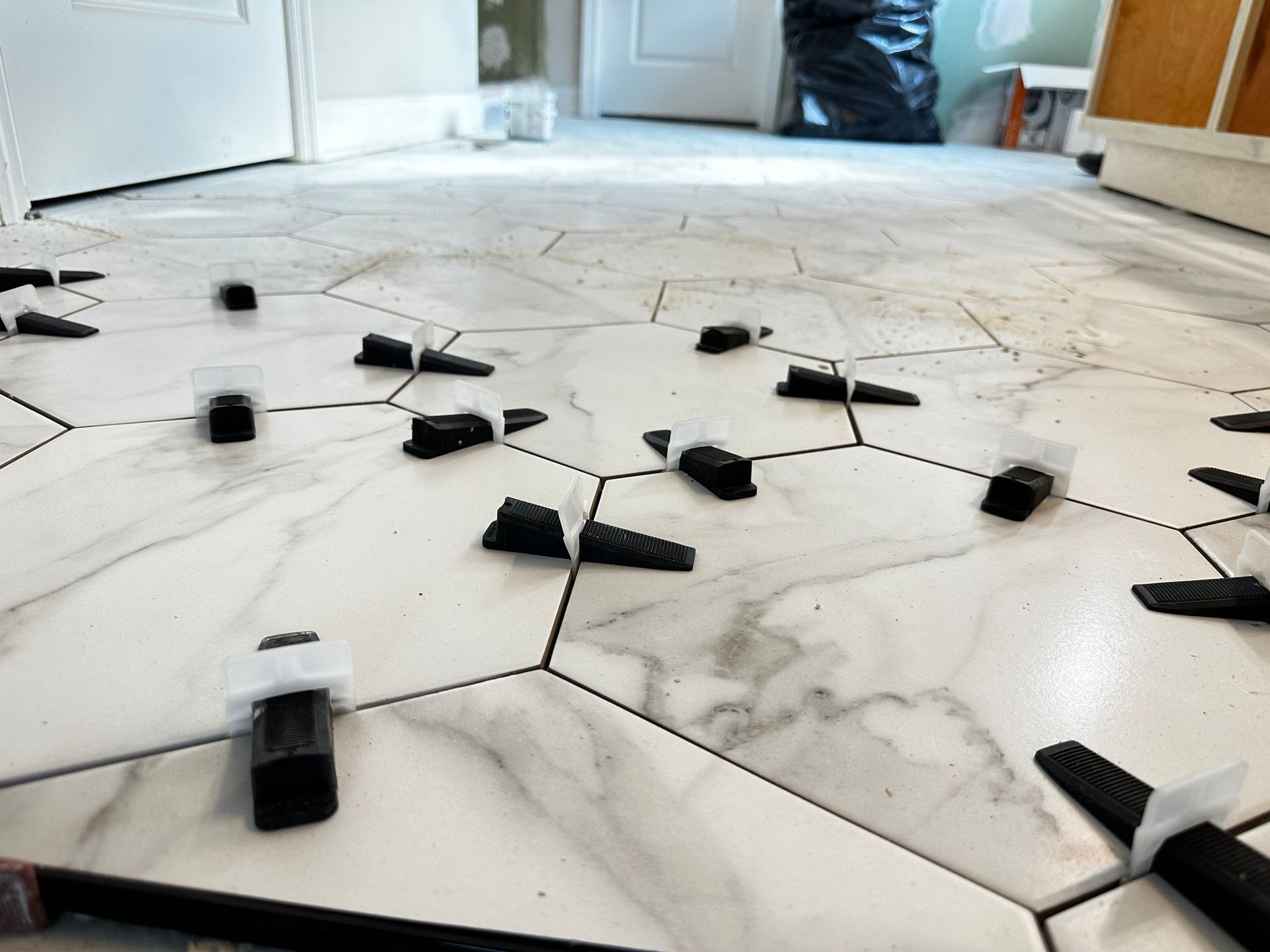 White marble hexagon tiles with leveling clips on a floor, likely during installation.