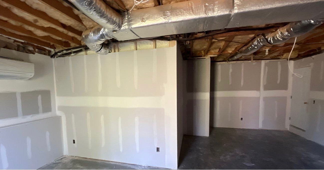 Interior of a room under construction, with drywall walls, exposed ceiling beams, and ductwork.