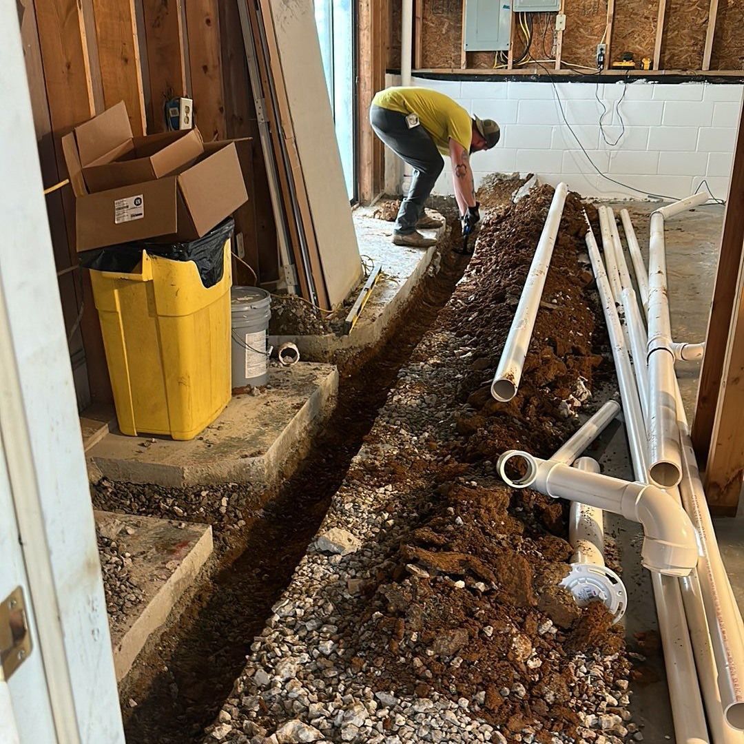 A person digs a trench in a basement, preparing for new plumbing.