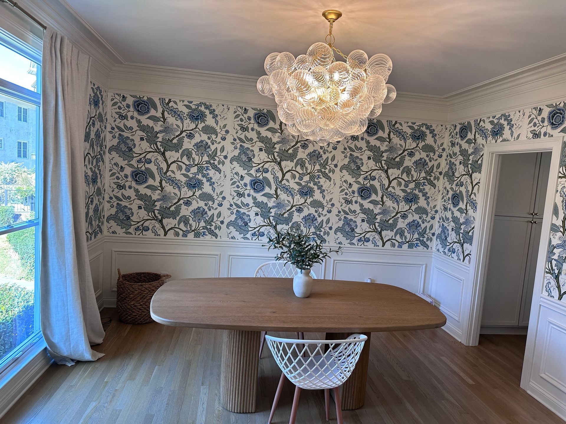 Elegant dining room with floral wallpaper, wooden table, and bubble chandelier.