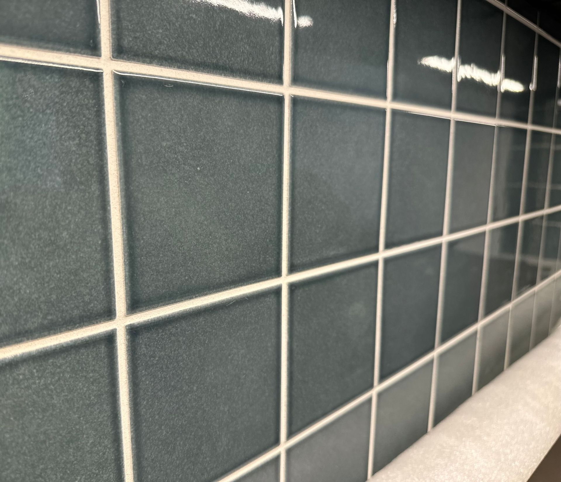 Close-up view of teal square tiles with white grout on a wall.
