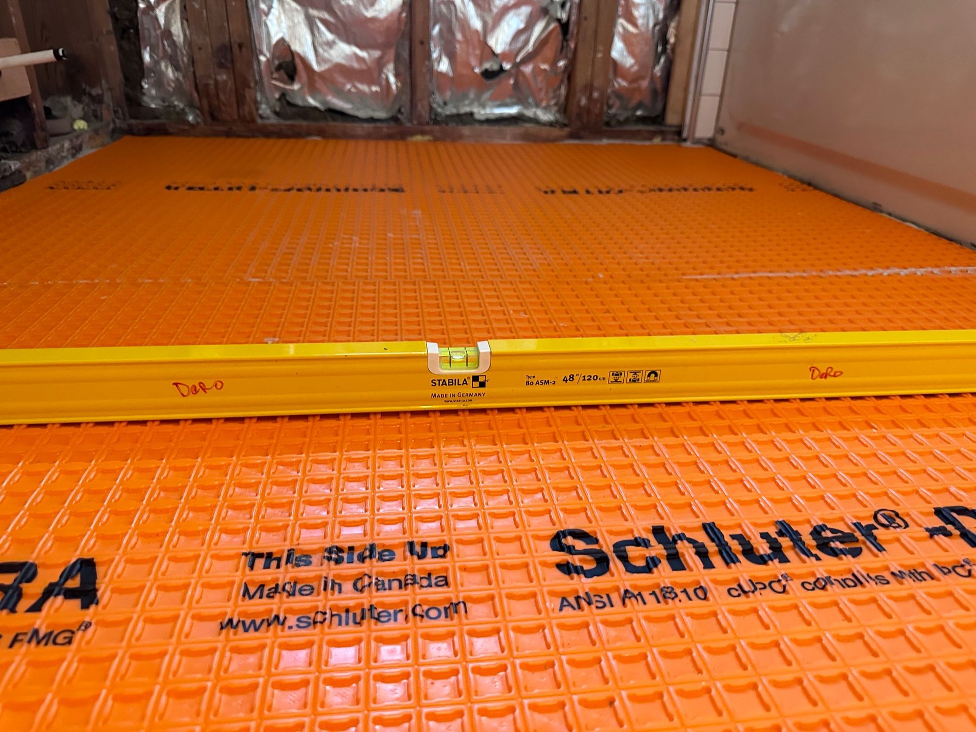 Orange Schluter Ditra membrane installed in a bathroom, with a yellow level resting on it.