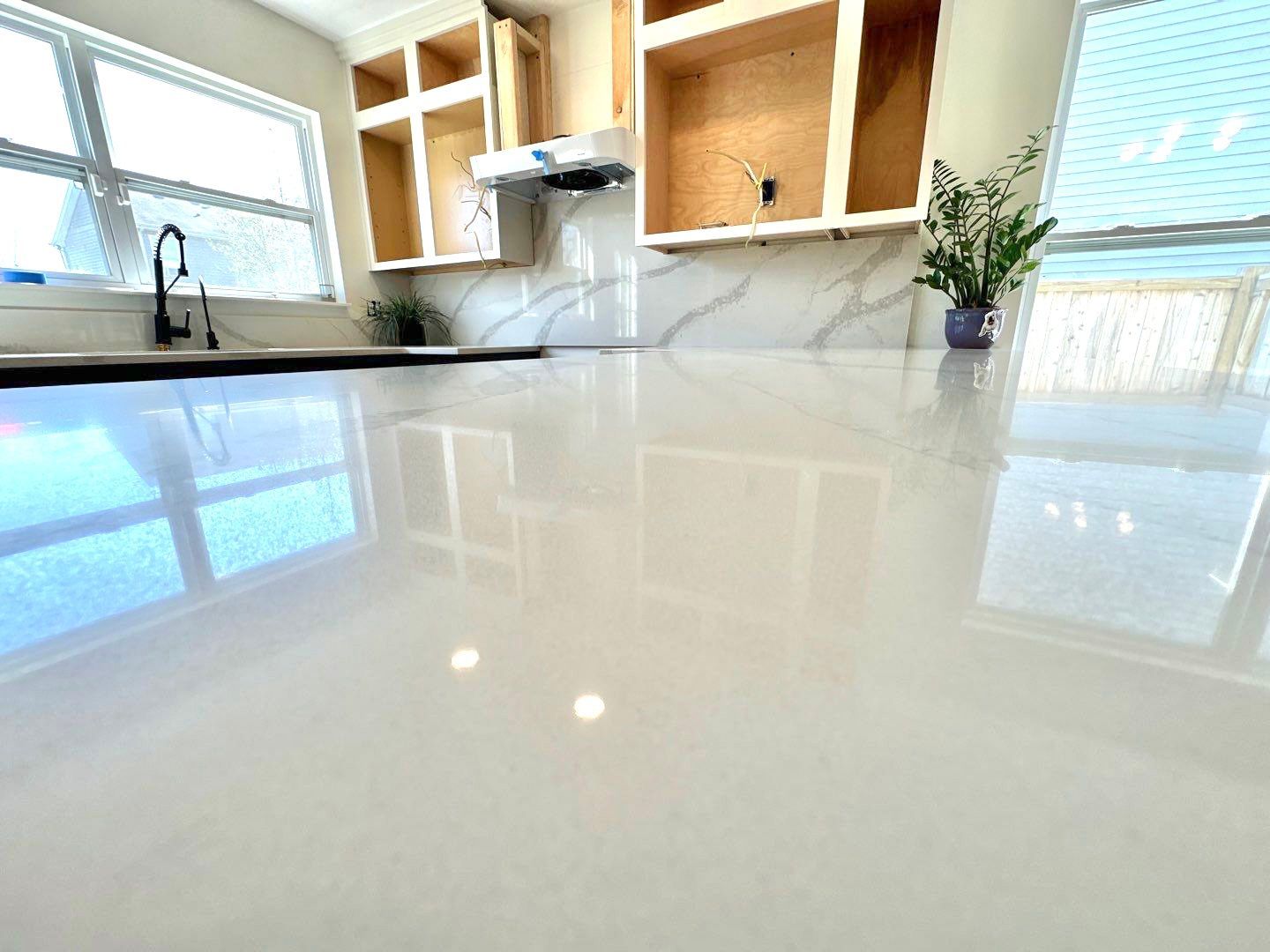 White kitchen countertop with unfinished cabinets, sink, and windows.