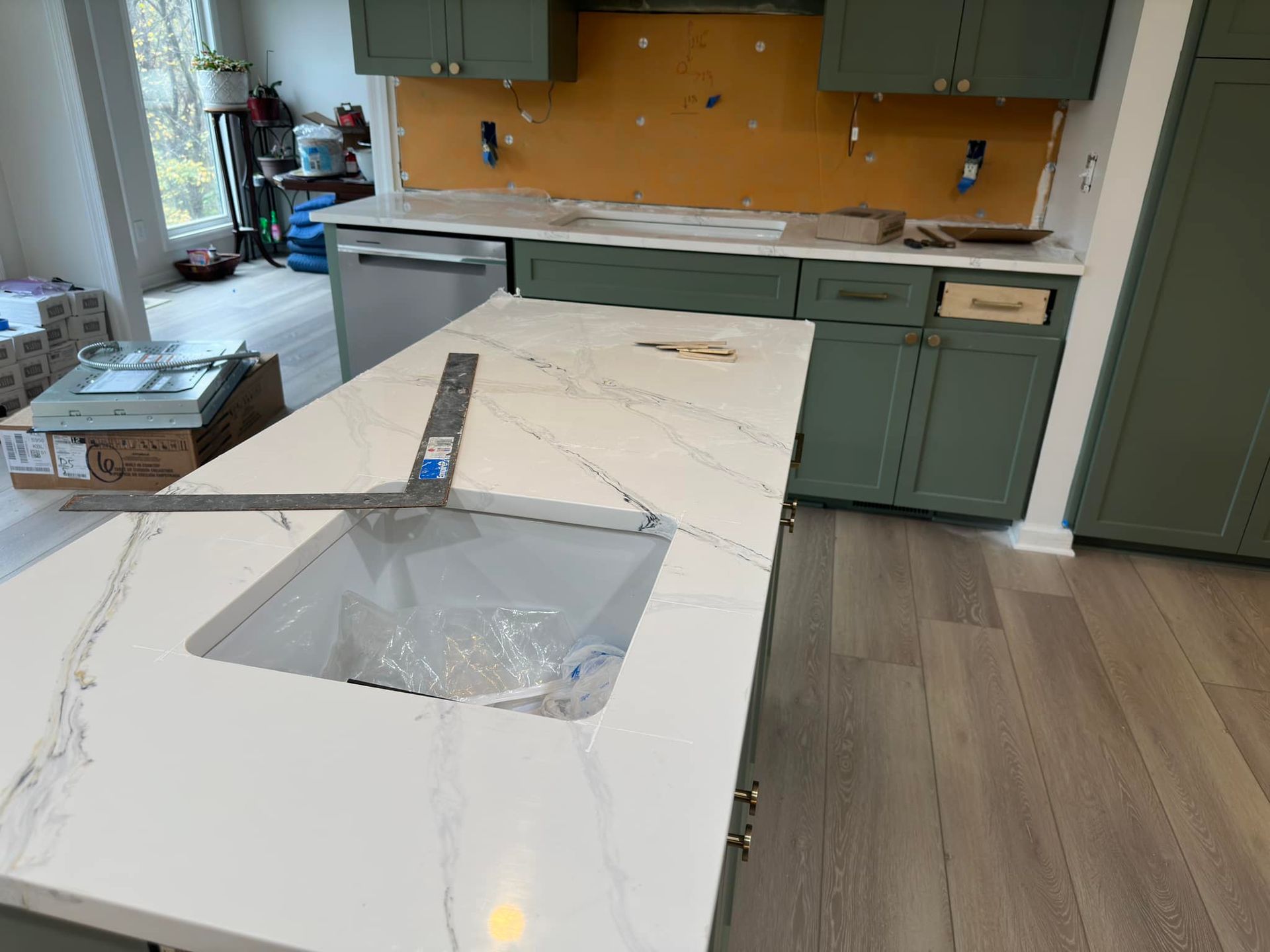 Kitchen under construction: white quartz countertop with sink, green cabinets, dishwasher, wood floors.