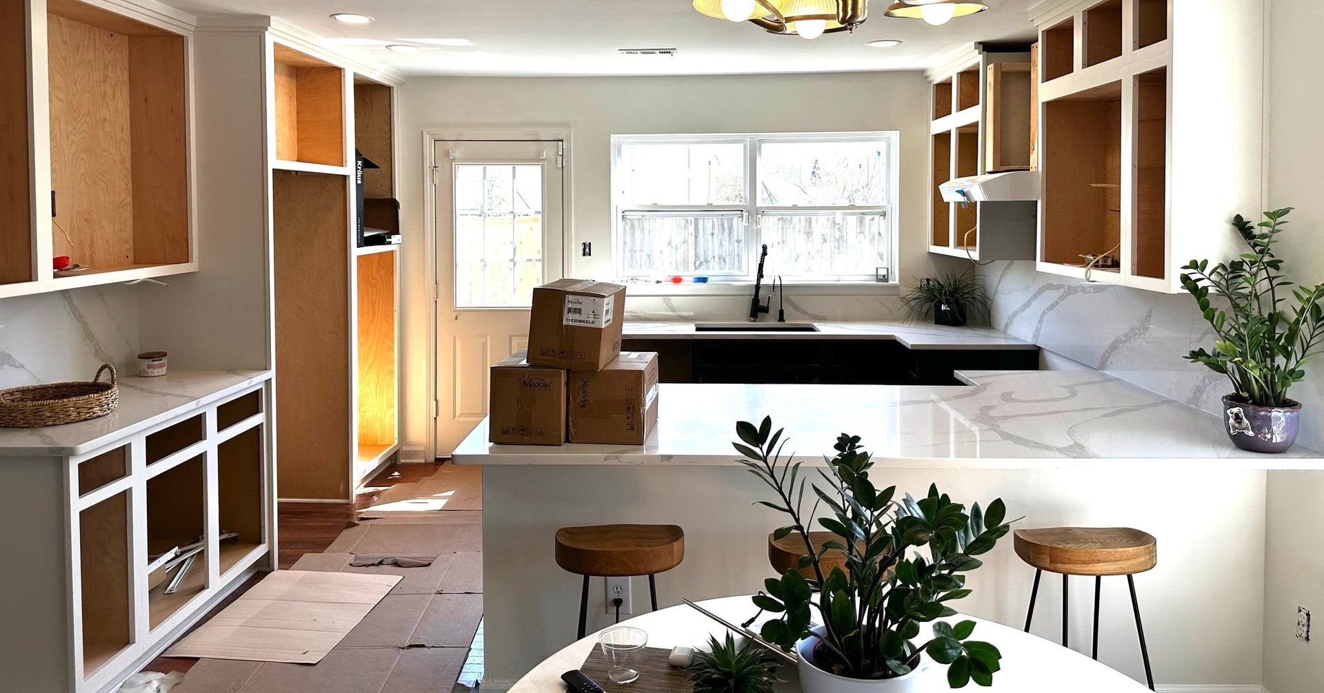 Kitchen under renovation with exposed cabinets, new countertops, and island with stools.