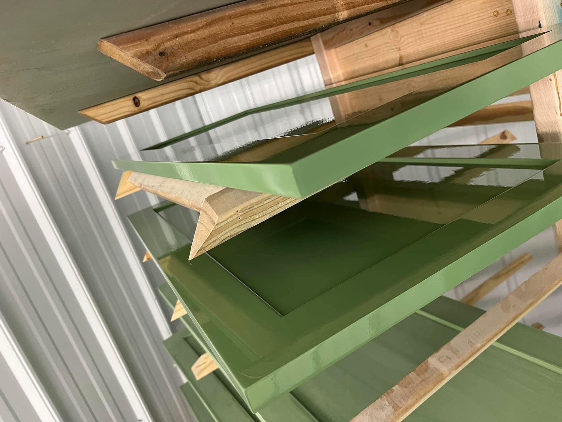 Green painted cabinet doors drying on wooden racks in a workshop.