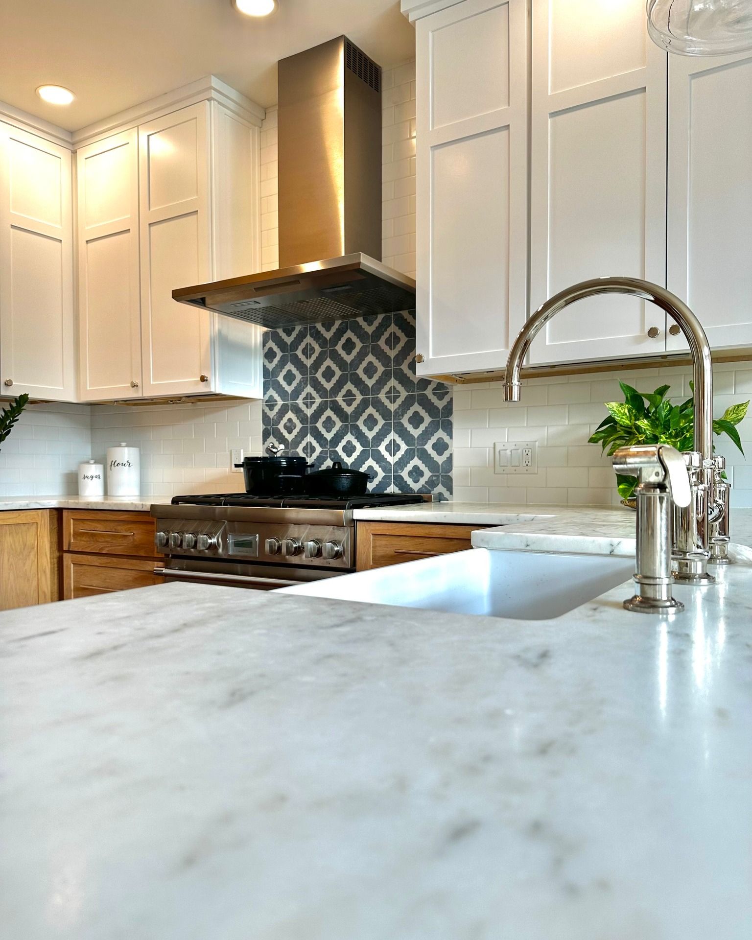Kitchen with white cabinets, marble countertop, stainless steel range hood, and blue and white tile backsplash.