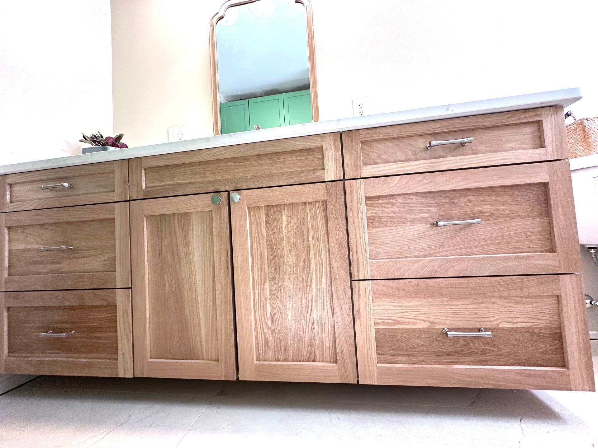 Wooden bathroom vanity with drawers and doors, topped with a white counter and mirror.