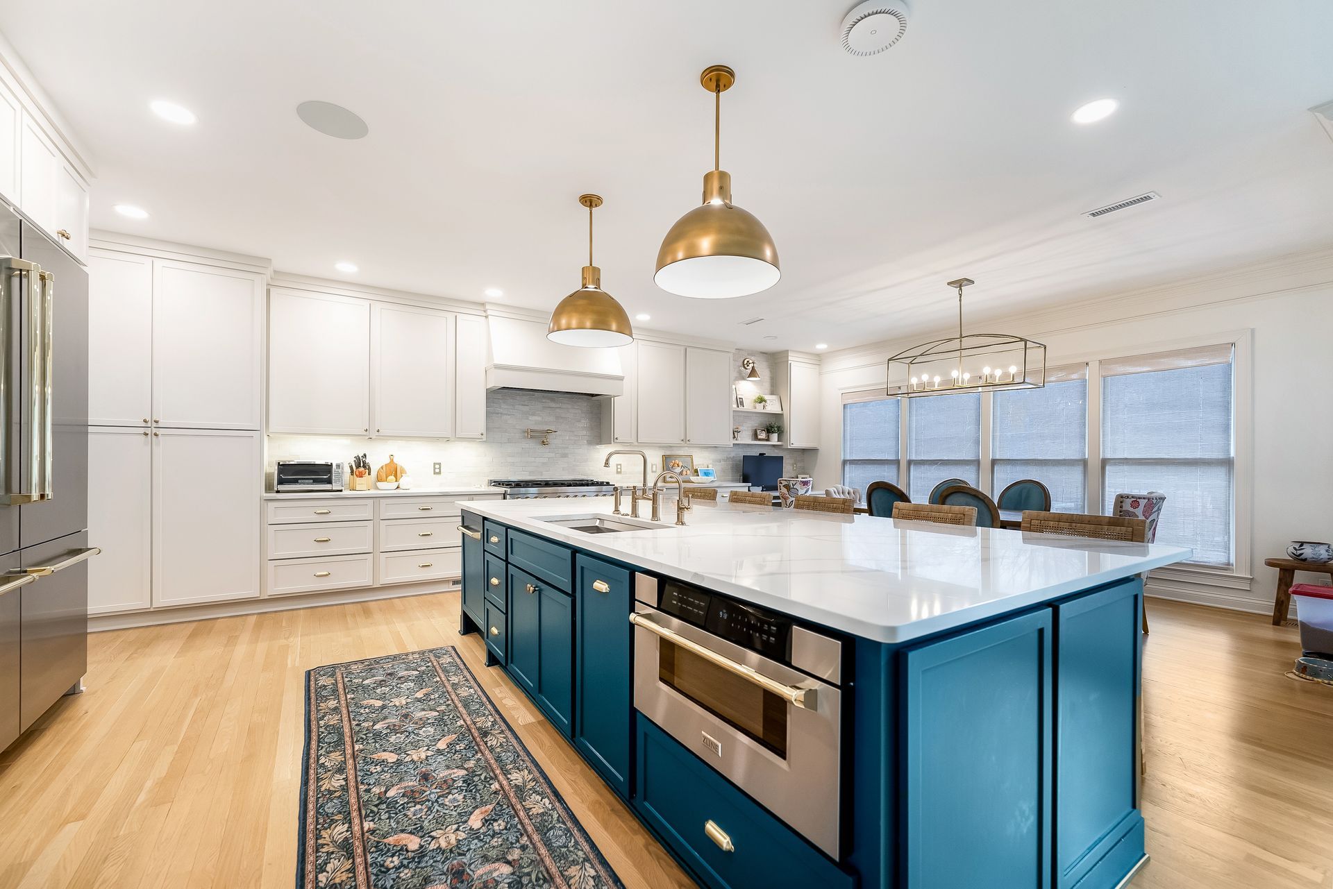 Spacious modern kitchen with blue island, white cabinets, gold pendant lights, and wood floors.