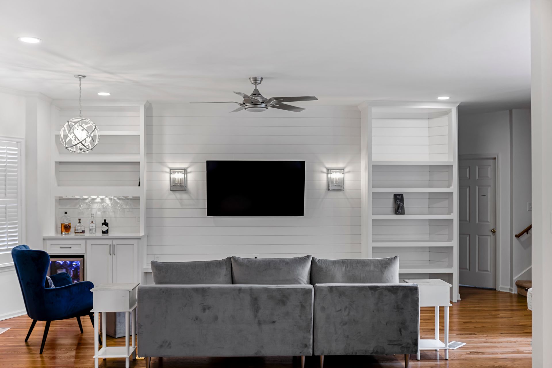 Living room with white shelves, a grey couch, TV, and a blue chair.