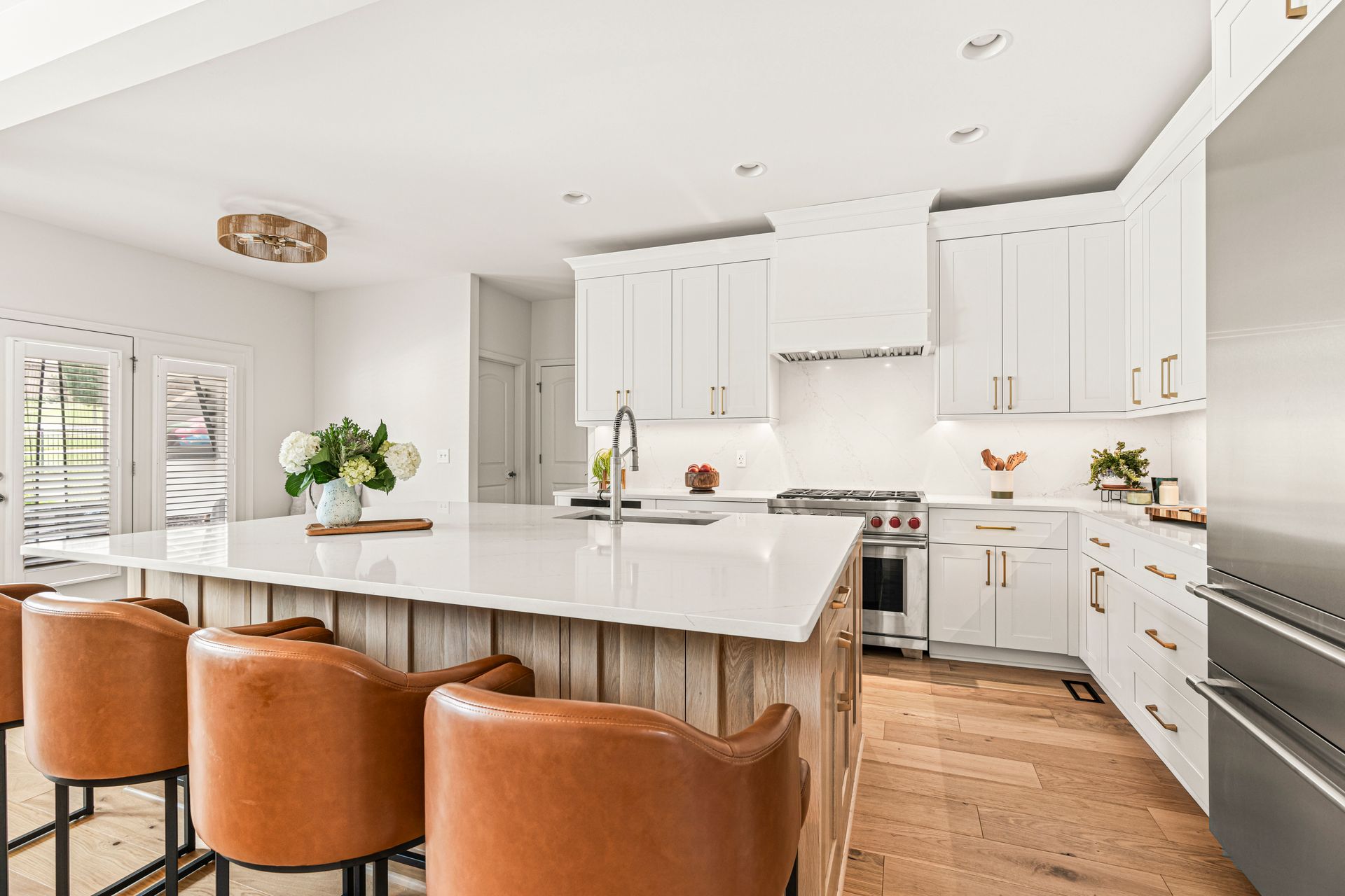Modern kitchen with white cabinets, large island with leather bar stools, and stainless steel appliances.