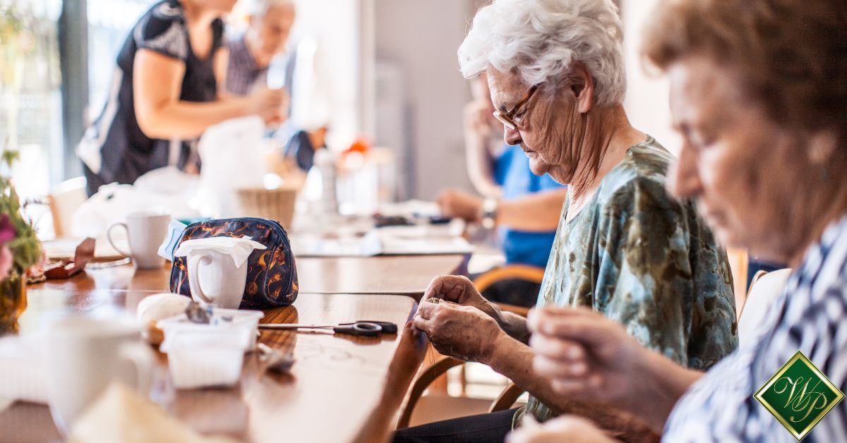 group of elderly women working on projects at a table - Whispering Pines assisted living