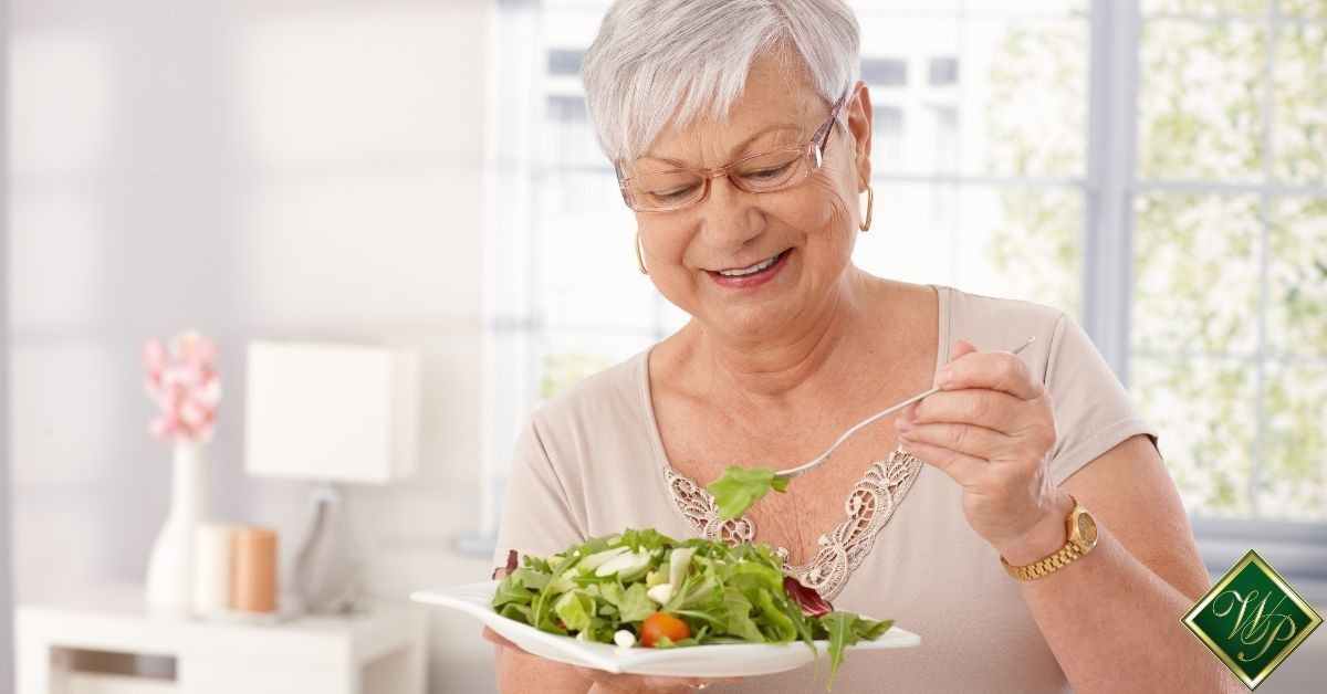 Smiling woman tossing salad in a bright kitchen with a bowl of greens