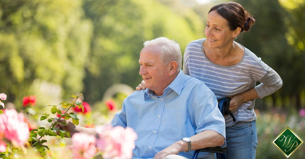 Two people in a garden, one seated and one standing behind, surrounded by colorful flowers