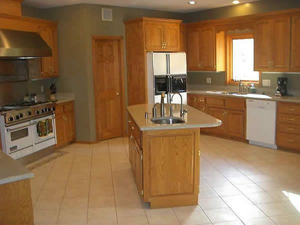 Spacious kitchen with wooden cabinets, central island, white appliances, and tiled floor.