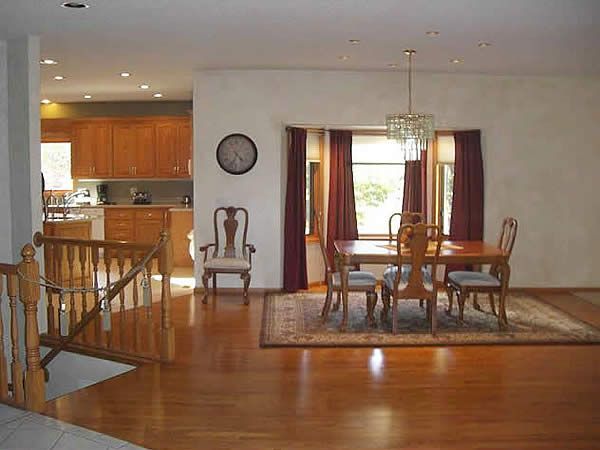 Bright dining room with wooden table, chairs, rug, and an open view to the kitchen.