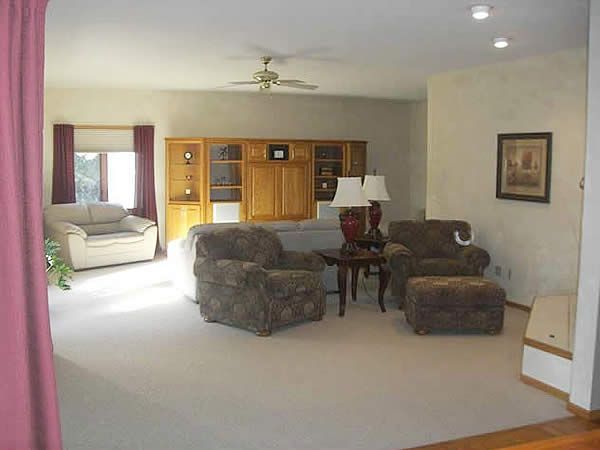 Spacious living room with beige carpet, brown sofas, wooden cabinet, lamp, and white armchair near a window.