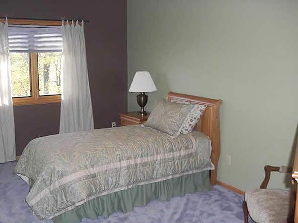 Small bedroom with a bed, lamp, window, and chair on a purple and green wall backdrop.