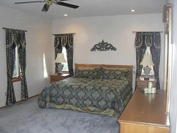 Bedroom with a large bed, ceiling fan, white walls, gray carpet, and matching curtains