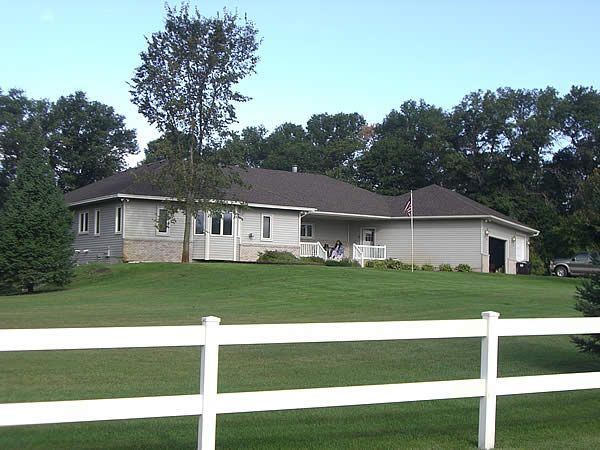 Suburban house with a white fence and green lawn under trees
