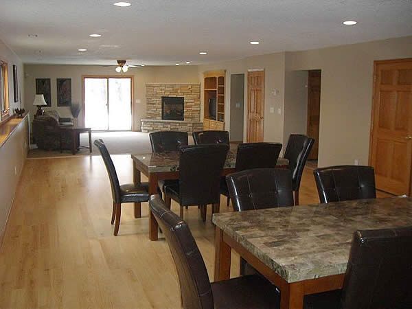 Open-concept living and dining room with wooden floors, dark chairs, and a stone fireplace.