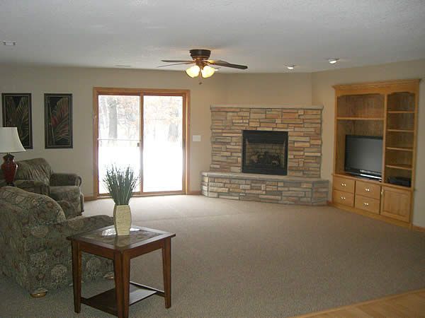 Spacious living room with stone fireplace, built-in TV shelves, carpet, and sliding glass doors.