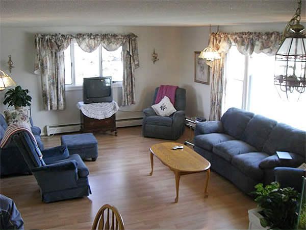 Living room with blue sofas, armchairs, TV, coffee table, and large windows with curtains