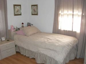 Small bedroom with an unmade bed, two framed pictures, a nightstand, and a window with curtains.