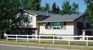 Suburban house with beige siding and white fence on a sunny street lined with trees