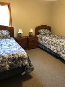 Small bedroom with two twin beds, nightstands, lamps, and a window with beige walls.