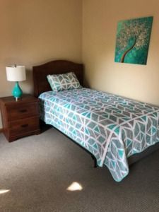 Small bedroom with a single bed, wooden nightstand, and turquoise lamp beside a teal wall print.