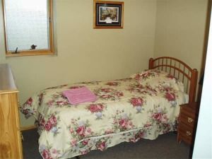 Small bedroom with floral bedspread, wooden headboard, nightstand, and window.
