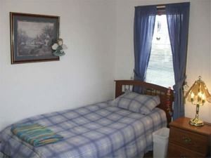 Small bedroom with a twin bed, blue curtains, framed wall art, and a bedside lamp.
