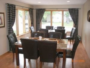 Dining room with dark chairs, wooden table, and large windows with checkered curtains.