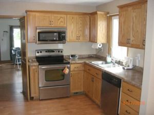 Small kitchen with wood cabinets, stainless steel stove and microwave, and a sink by the window.