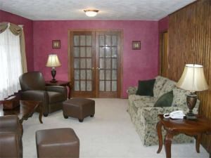 Cozy living room with pink walls, floral sofa, leather chair, lamps, and French doors.