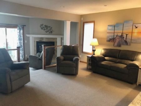 Cozy living room with fireplace, dark armchair, sofa, lamp, and beach artwork on the wall