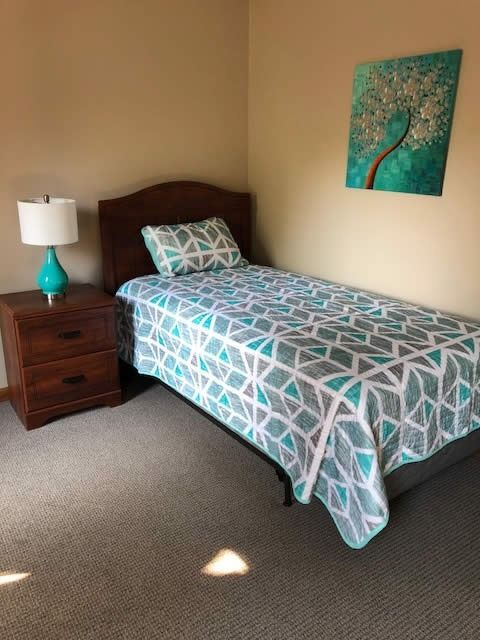 Bedroom with a single bed, teal lamp, wooden nightstand, and abstract wall art.