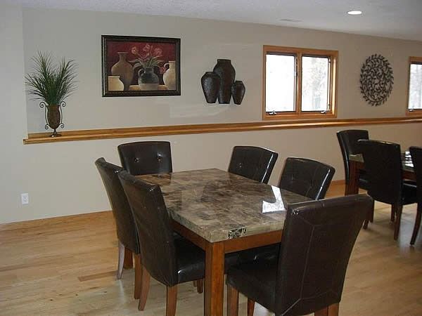 Dining room with wooden table and dark chairs beside a wall shelf and window.