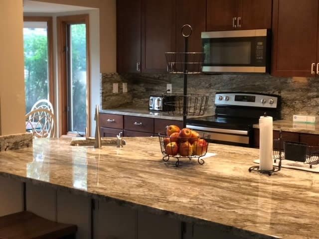Modern kitchen with granite island, dark cabinets, stainless appliances, and a fruit bowl by patio doors