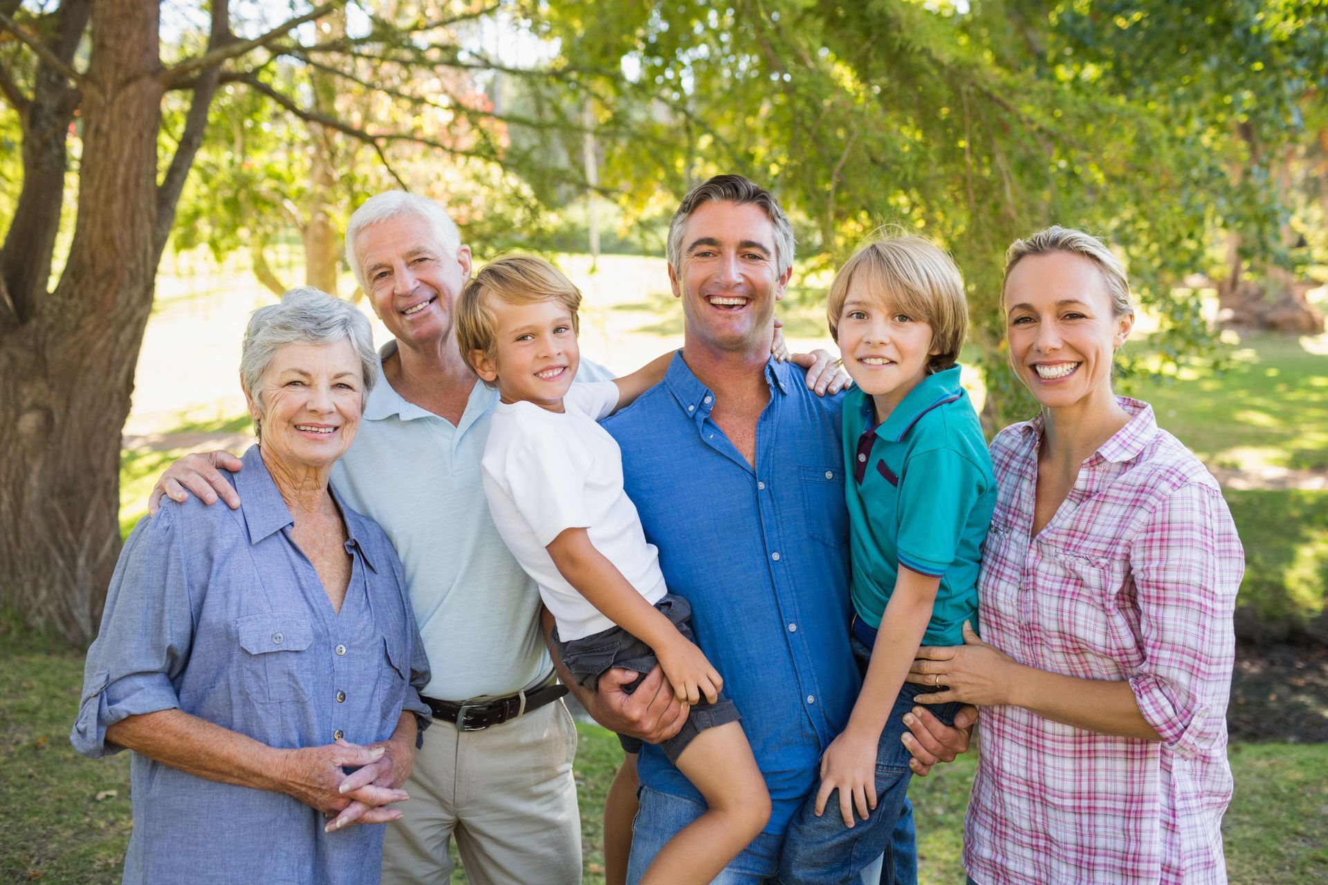 Smiling family group standing together outdoors in a sunny park with trees in the background
