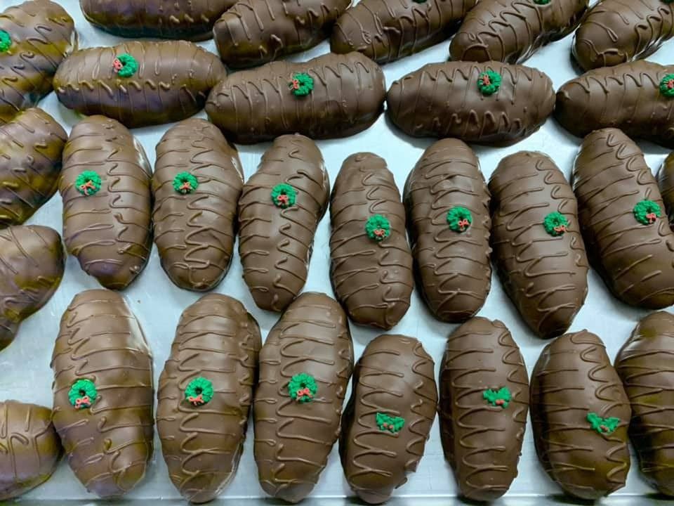 Tray of chocolate-covered pastries, oval-shaped with green decorative frosting on top, on a light surface.