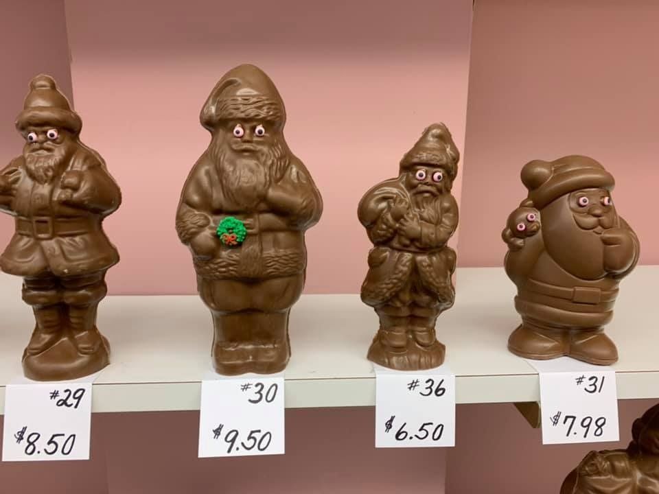 Four chocolate Santa figures on a shelf with prices listed below.