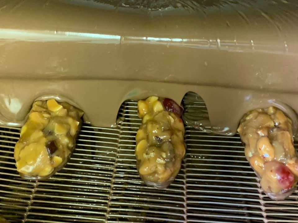 Three confections covered in chocolate on a wire rack, with flowing chocolate above.