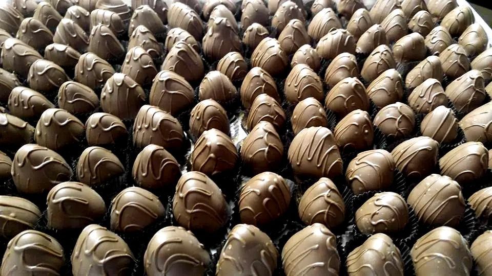 Rows of chocolate-covered strawberries, drizzled with white chocolate, on a dark tray.