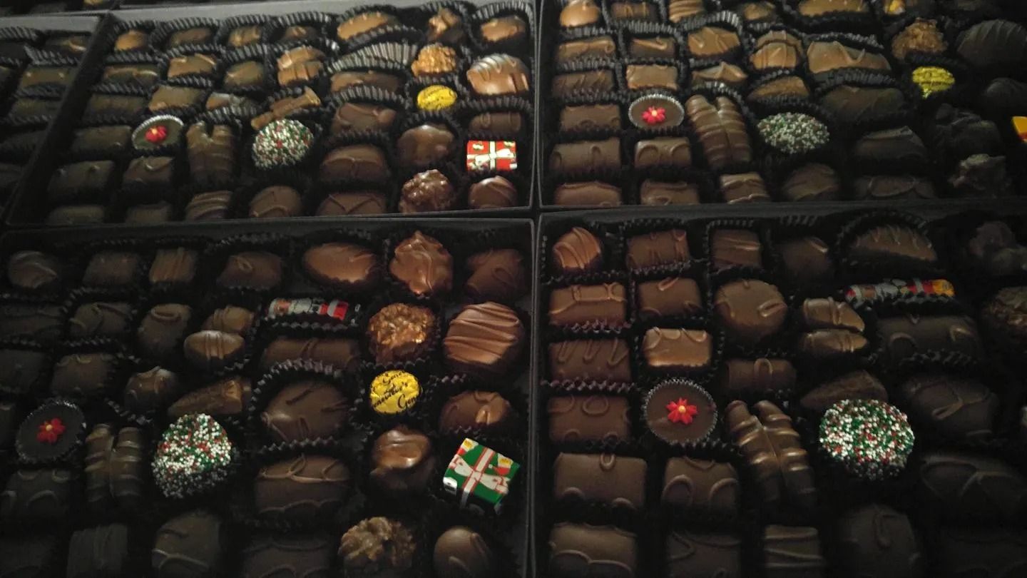 Assortment of chocolates in a box, various shapes and textures, shades of brown, some with colorful decorations.